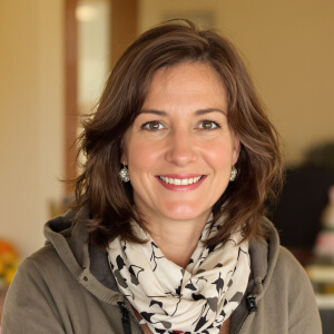 Smiling person with brown hair, wearing a scarf and a jacket, posed indoors.